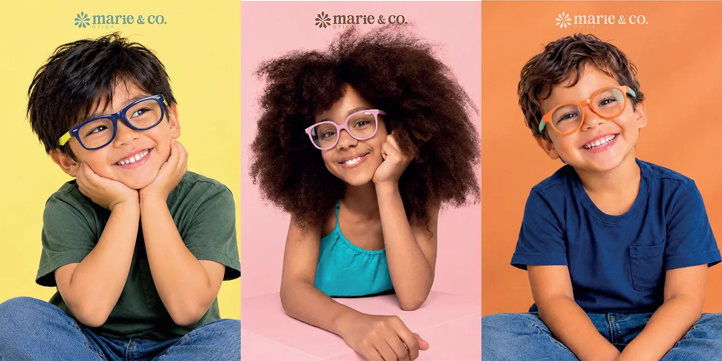 Três crianças sorrindo usando armações infantis coloridas da Óticas Marié
